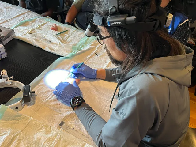 Person wearing magnifying headgear working on a small object with precision tools.