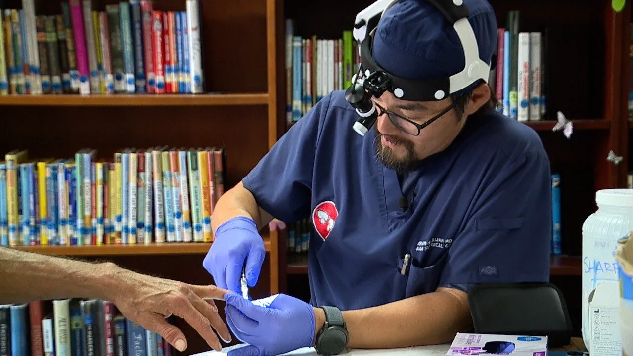 Dr. Aram, wearing a magnifying headlamp and gloves, treats a patient's hand at a volunteer clinic (ABC 10News story).