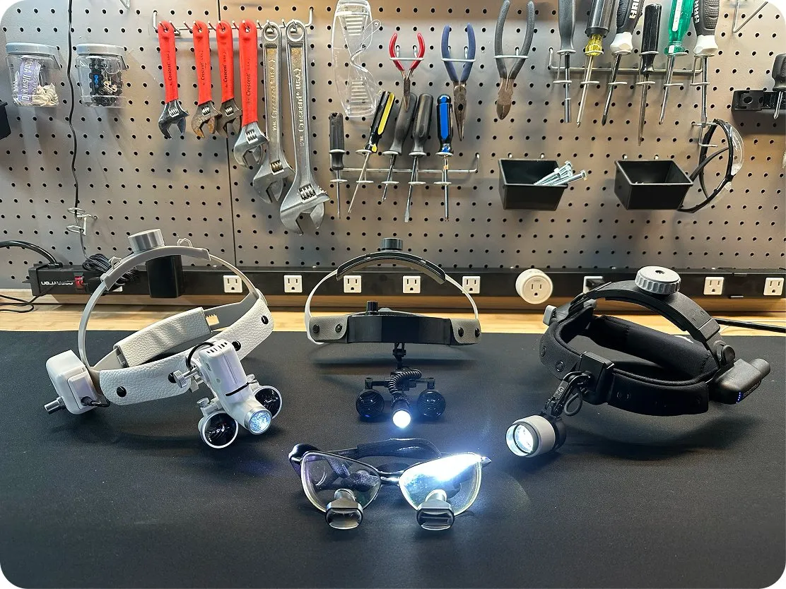 Headlamps and loupes lined up on a workbench, from lower to higher quality