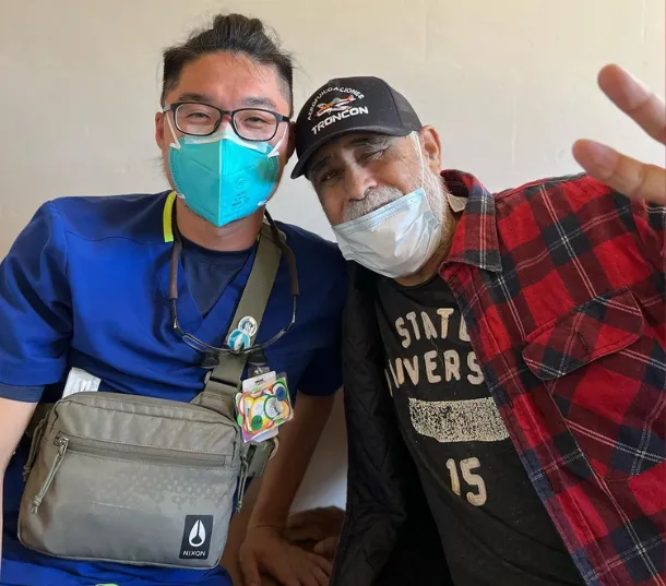 Two people wearing face masks, posing and smiling indoors.