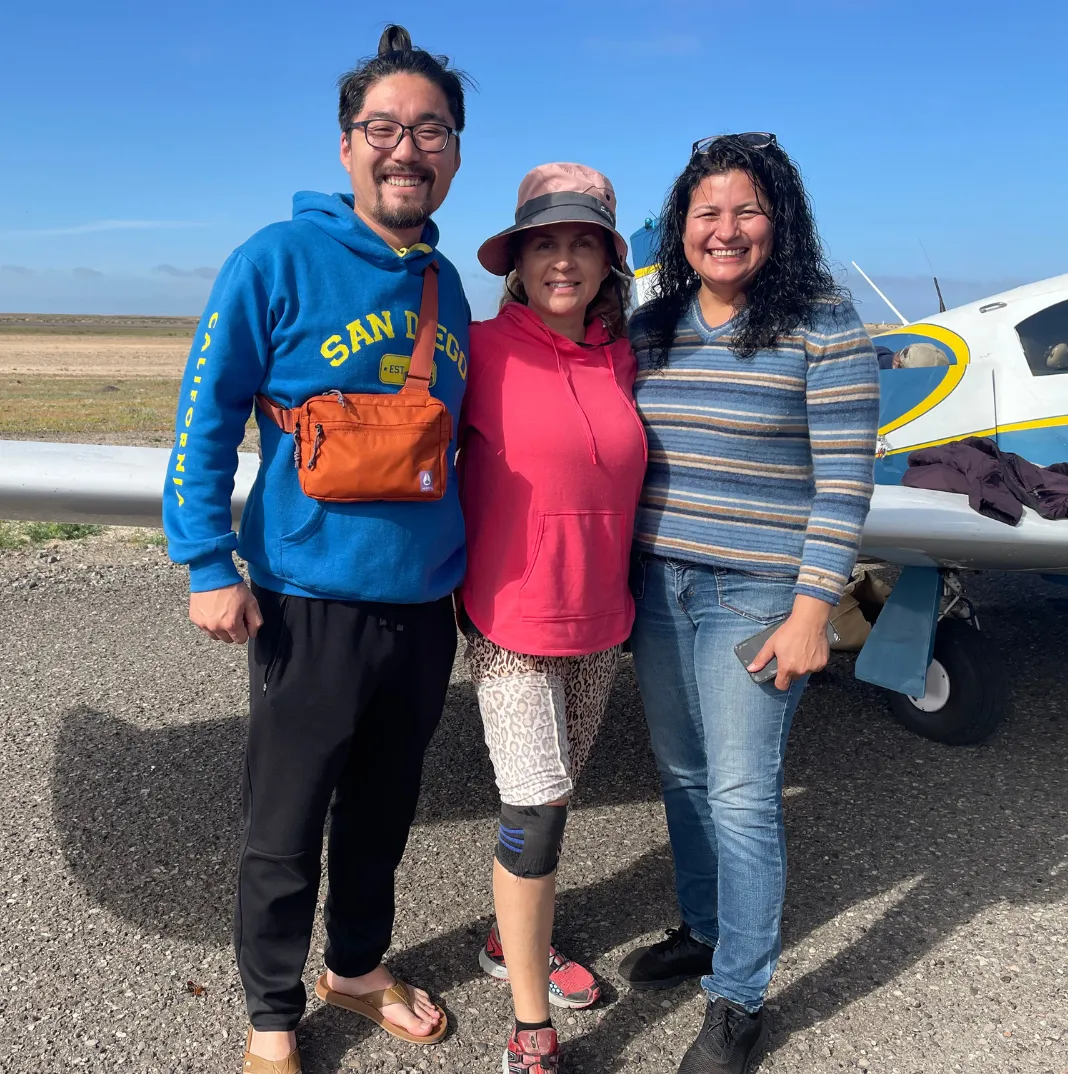 Three people standing next to a small airplane on a tarmac.