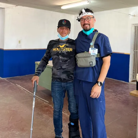 A man with a cane stands next to a smiling doctor in blue scrubs.