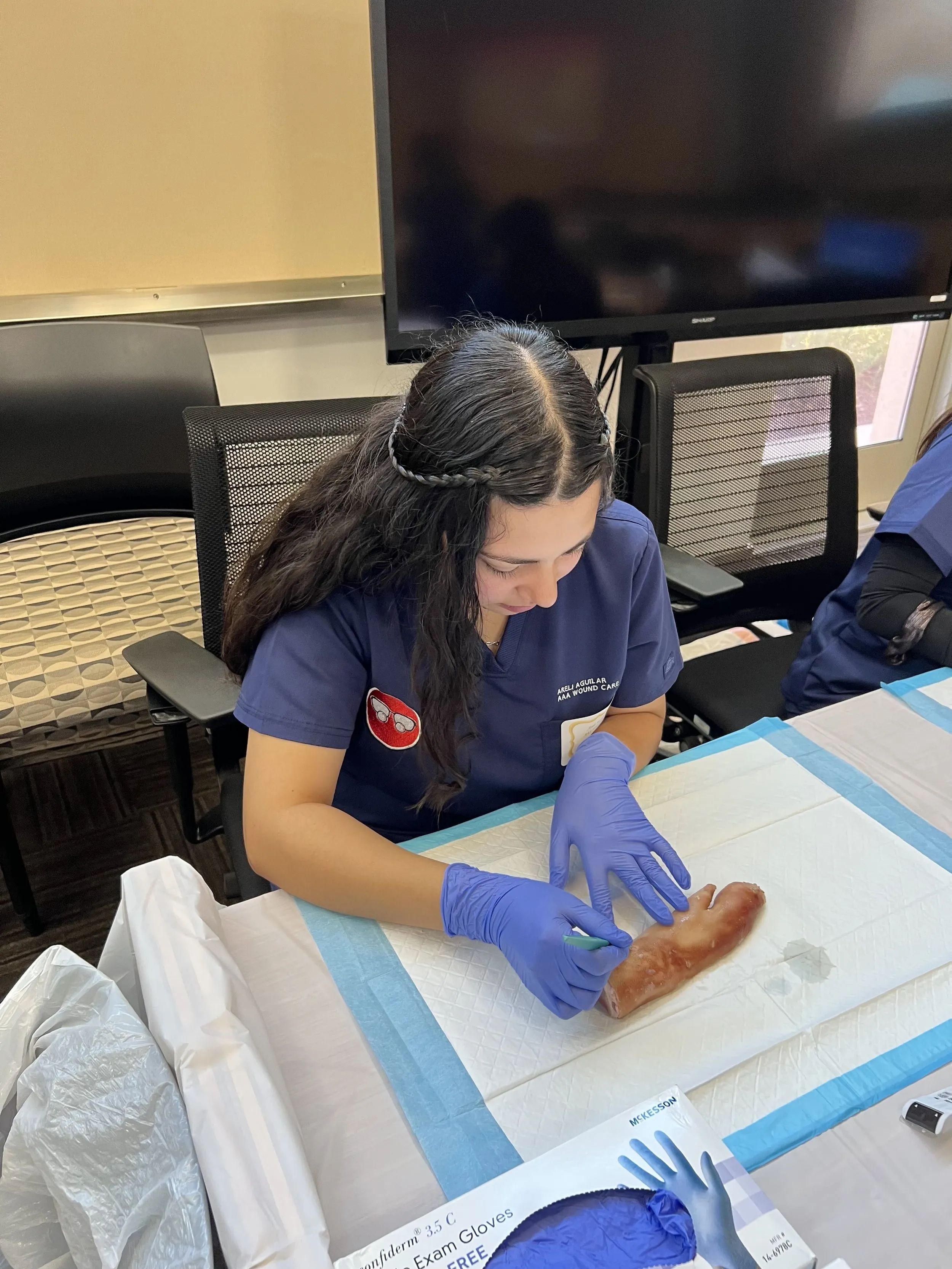 A person wearing blue medical scrubs is practicing a medical procedure on a simulation model.
