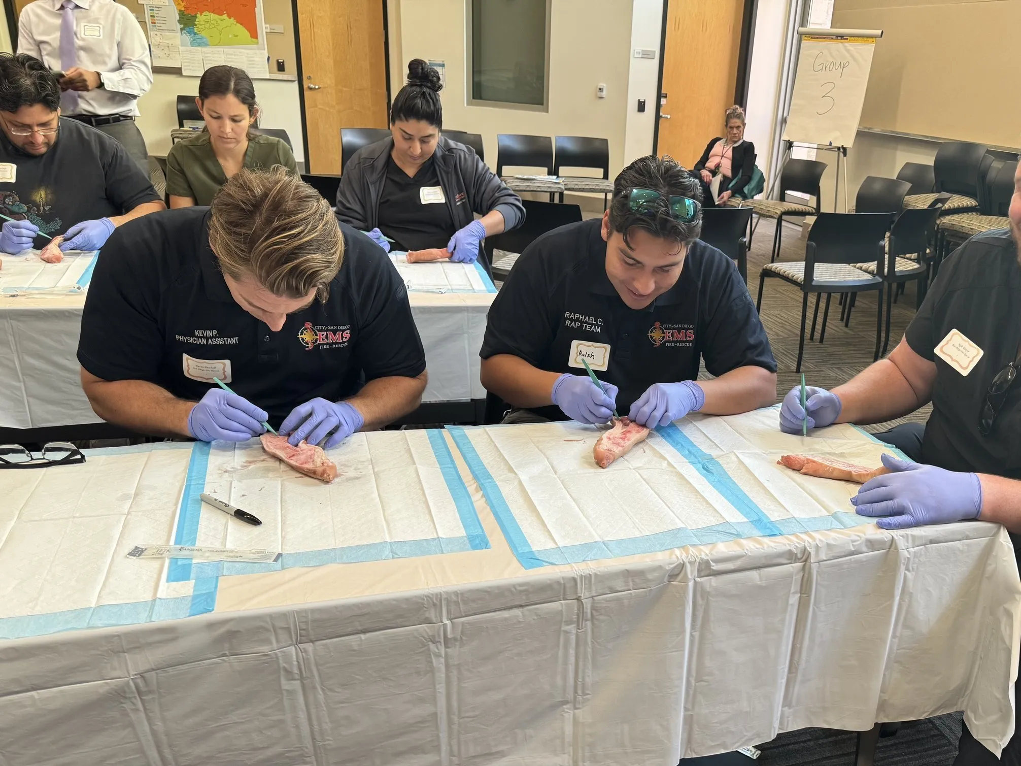 People wearing gloves practicing suturing on raw meat during a training session.