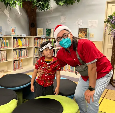 A child and an adult wearing a red Santa hat and a face mask.