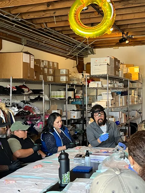 Wound care doctor demonstrates procedure using gloves and tools, while others observe.