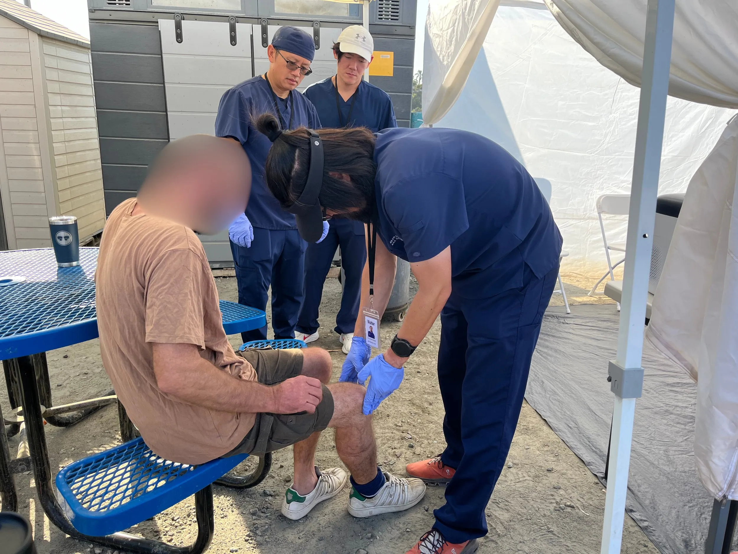 A AAA Wound Care provider treating a seated patient's leg at an outdoor clinic in downtown San Diego.