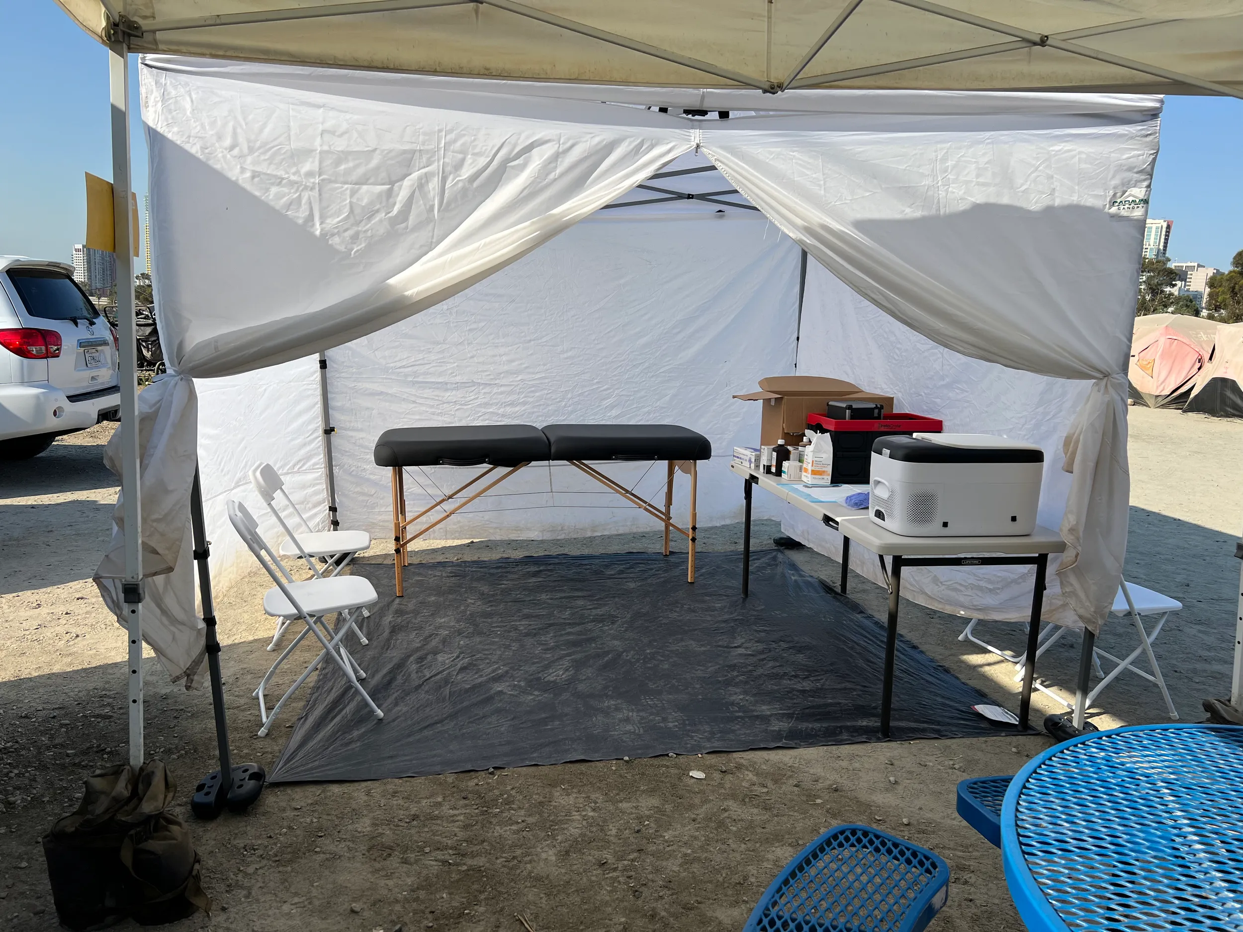 Outdoor medical tent setup with a massage table, chairs, and medical supplies.